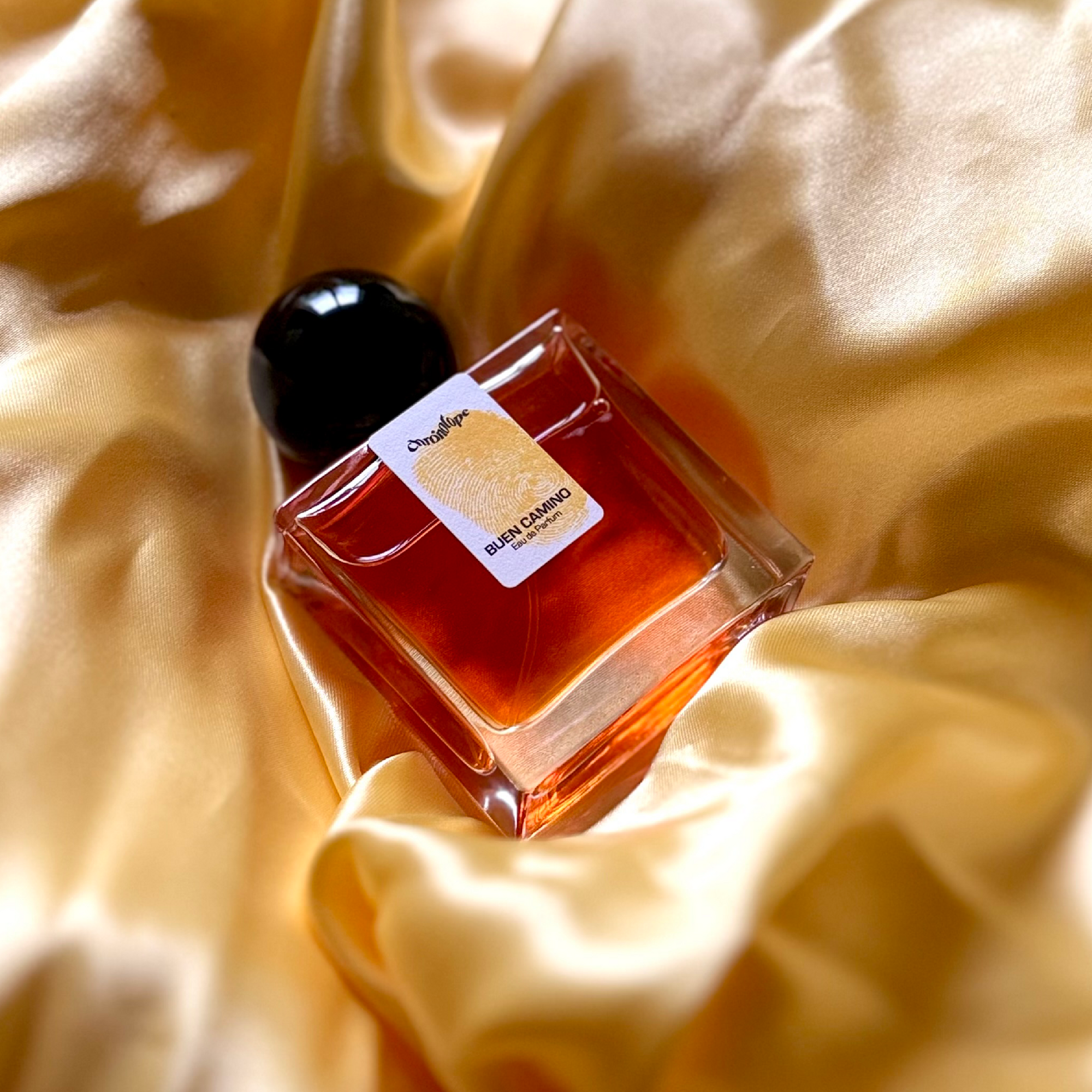 A bottle of Buen Camino Eau de Parfum by Chronotope, rests tenderly on an incoming tenderly among a flood of silklra flood of