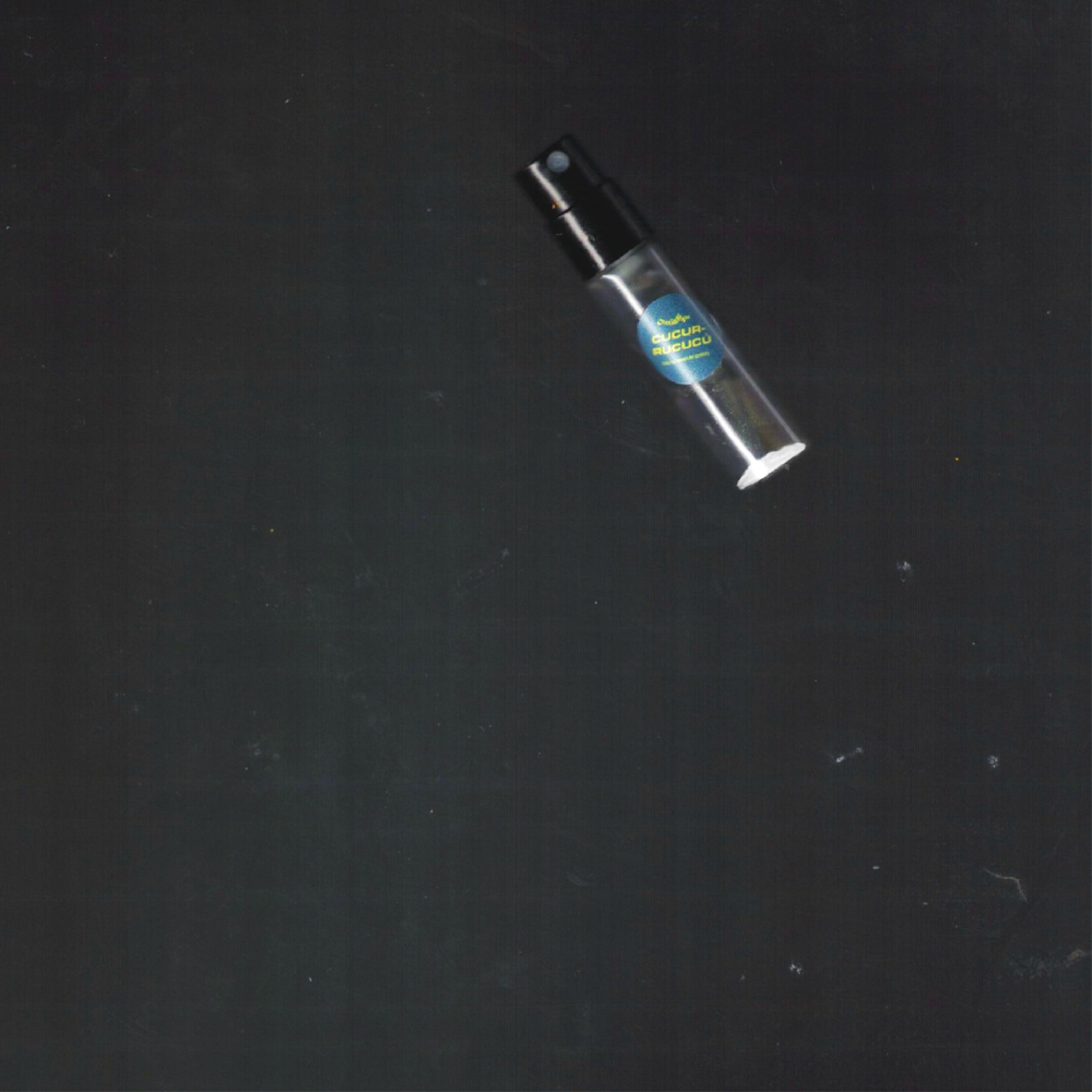 2mL spray sample of Chronotope Perfume’s Cucurrucucú Eau de Parfum with a hunter green label and silver enameled tip, set against a deep gray surface.