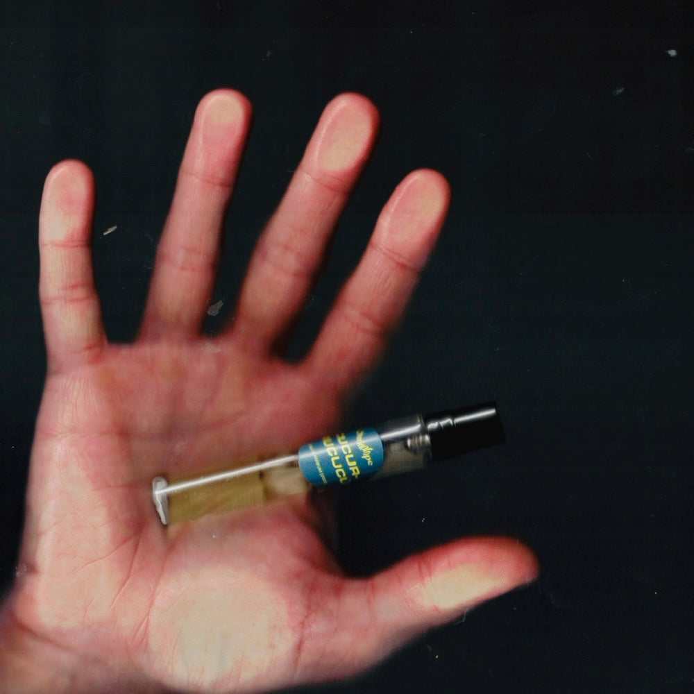 Hand holding a 7.5 mL travel spray of Chronotope Perfume’s Cucurrucucú Eau de Parfum, an avant-garde woody-incense fragrance featuring genuine copal negro essential oil, orris, and notes of ink, smoky mezcal, and absinthe.