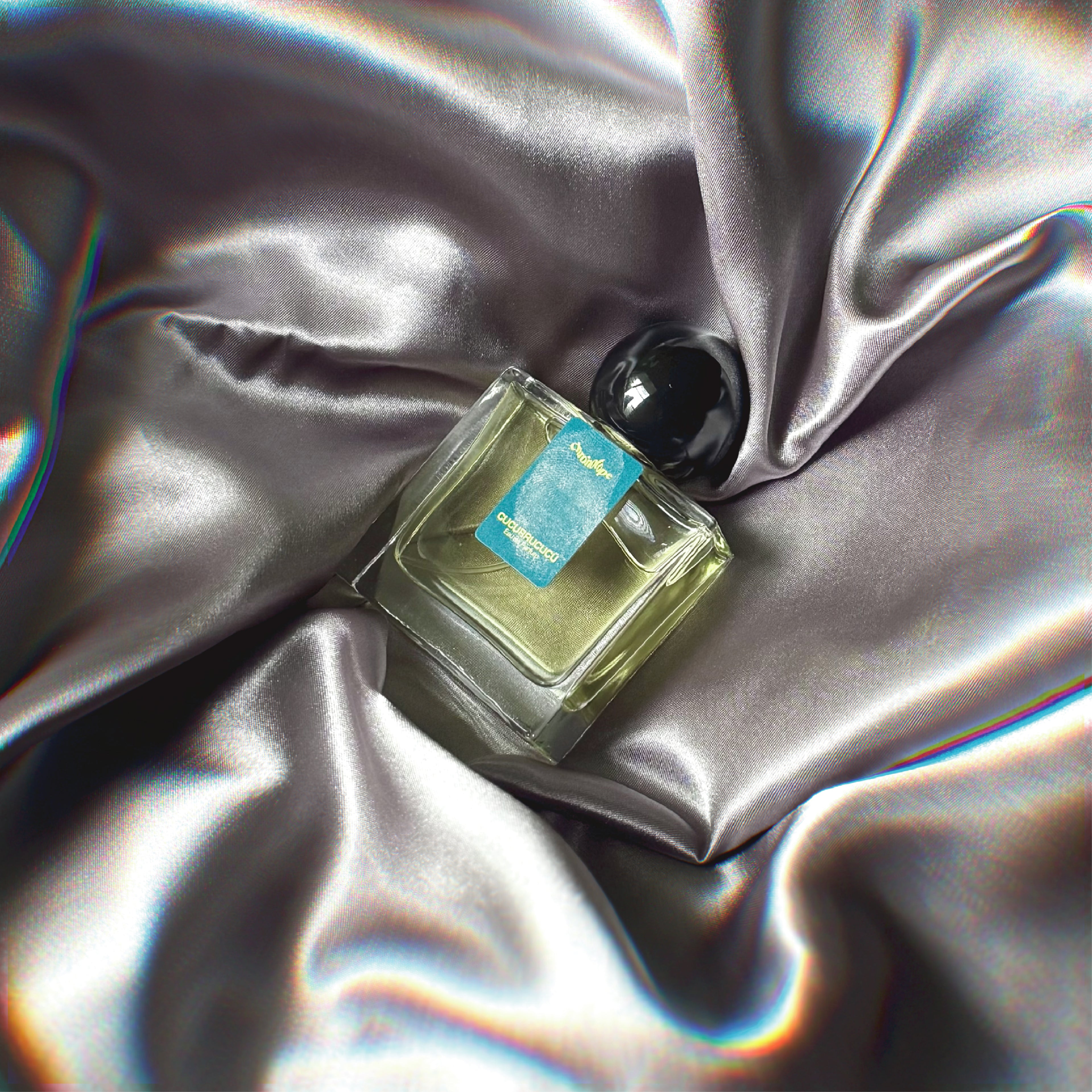 Chronotope perfume’s Cucurrucucu EdP lies in a shimmering nest of fabric in the same gunmetal silver-grey color as the thumbprint on the perfume bottle’s label.