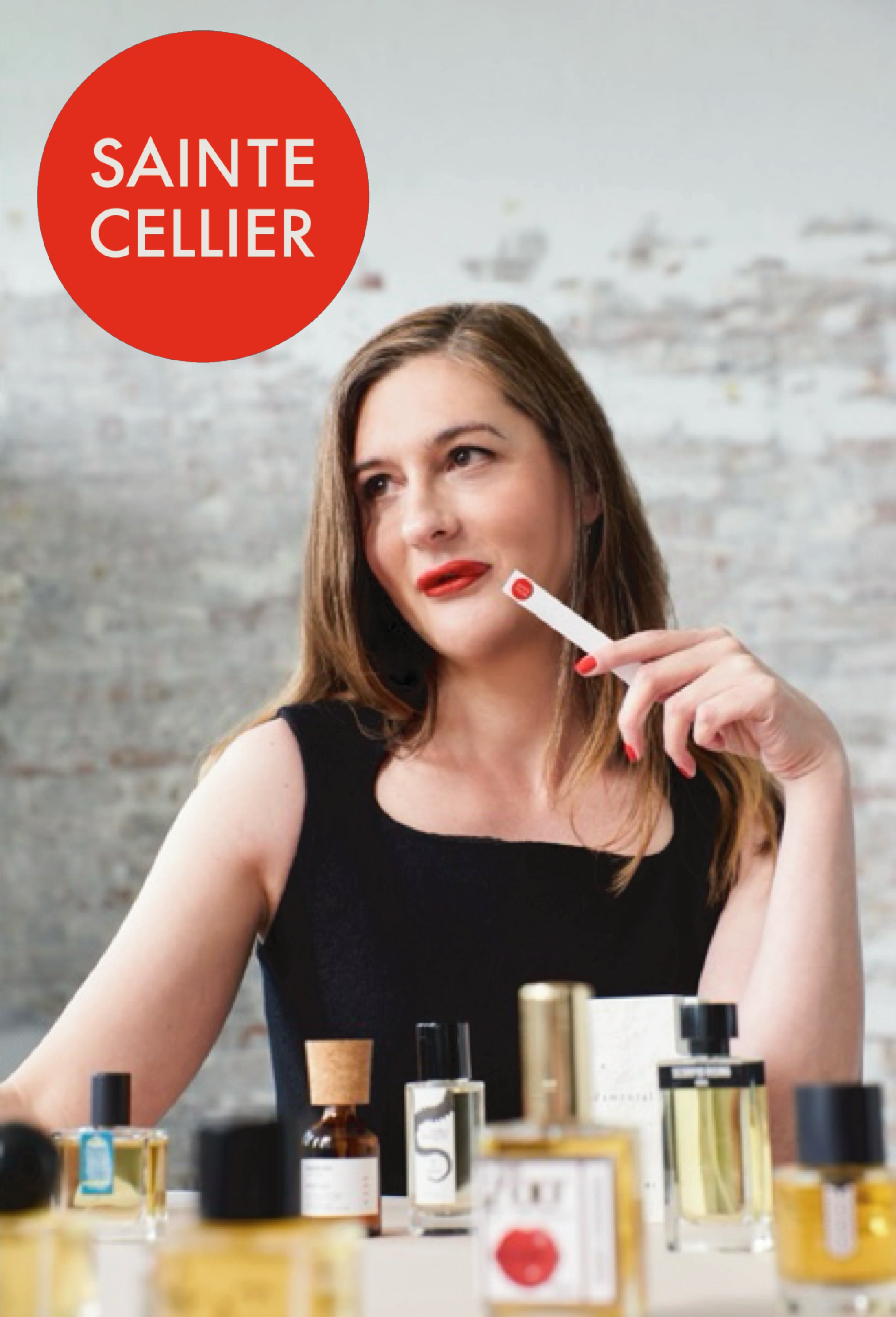 Brooke Belldon, founder of Sainte Cellier, sits before an array of perfume bottles on a table, one of which is Chronotope’s own Cucurrucucú Eau de Parfum.
