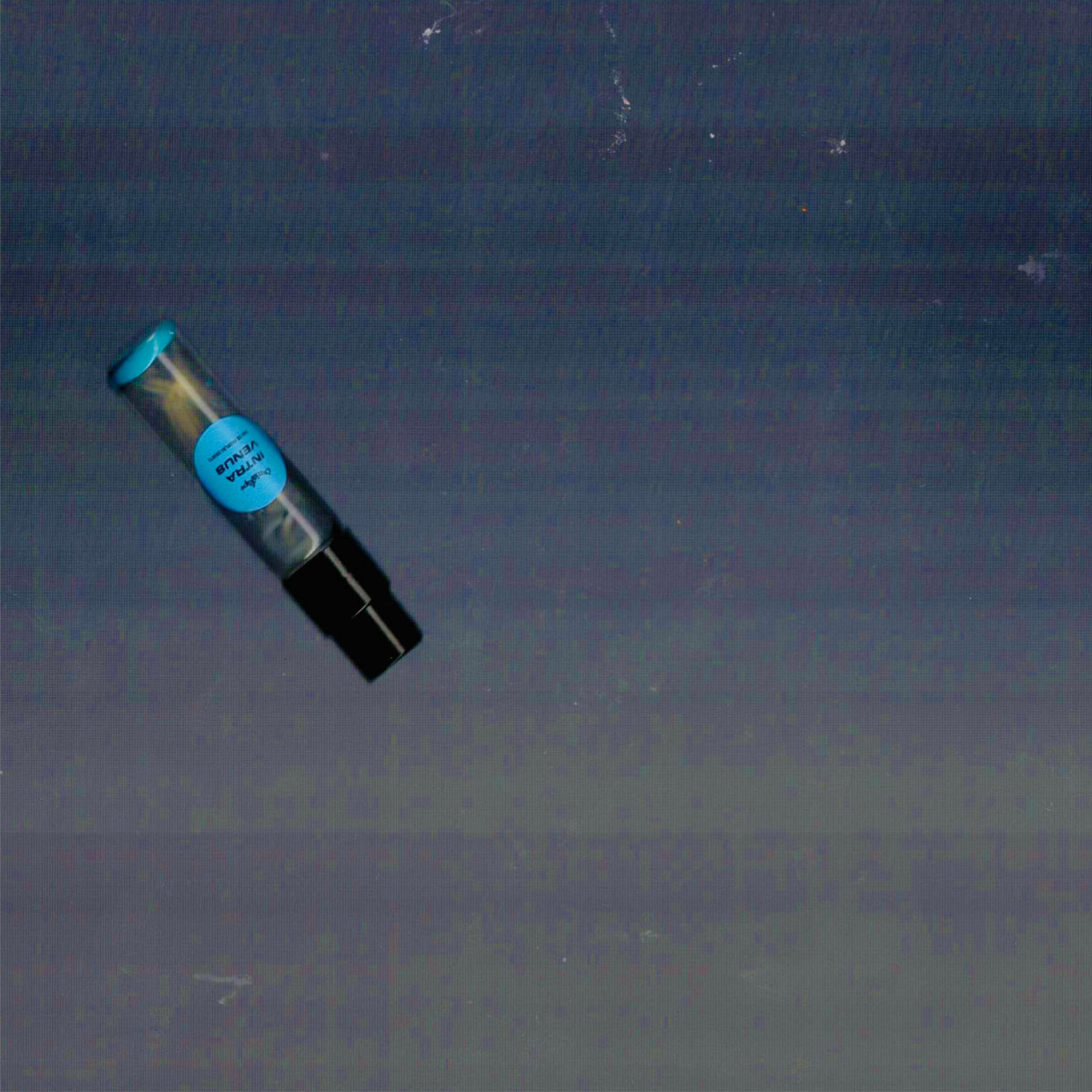 2mL spray sample of Chronotope Perfume’s Intra Venus Eau de Parfum with Hospital Blue label and matching enameled tip, floating over a smoky blue-gray background.