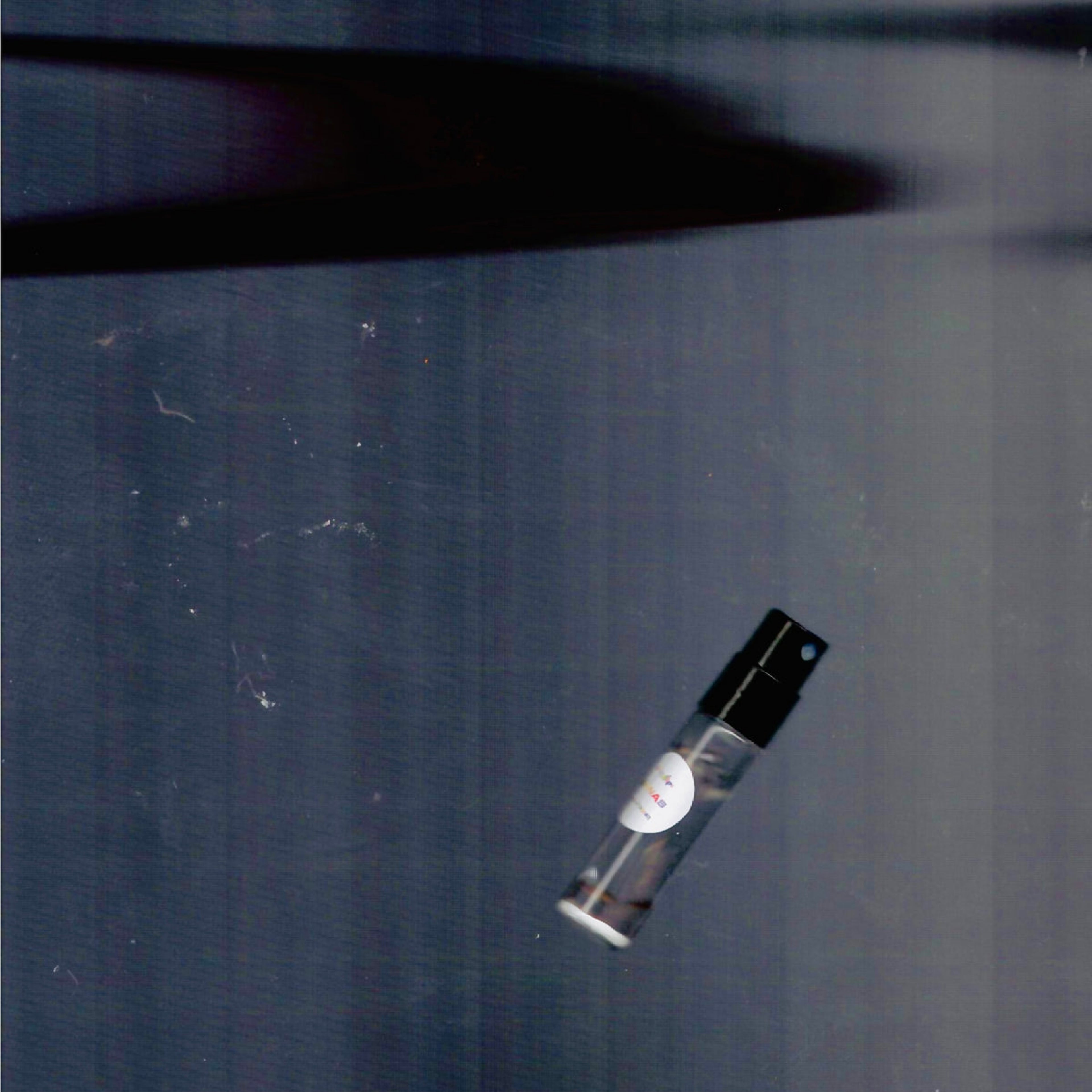 2mL spray sample of Chronotope Perfume’s Nanas Eau de Parfum with Banana White label and fluorescent pink enameled tip, resting on a shadowed gray background.