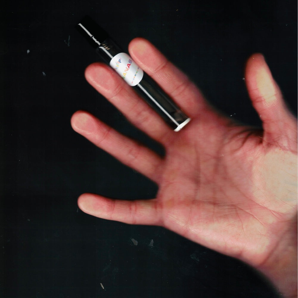 Hand holding a 7.5 mL travel spray of Chronotope Perfume’s Nanas Eau de Parfum, a joyful avant-garde fragrance featuring notes of banana candy, shiso, cardamom, and soft creamy sweetness.