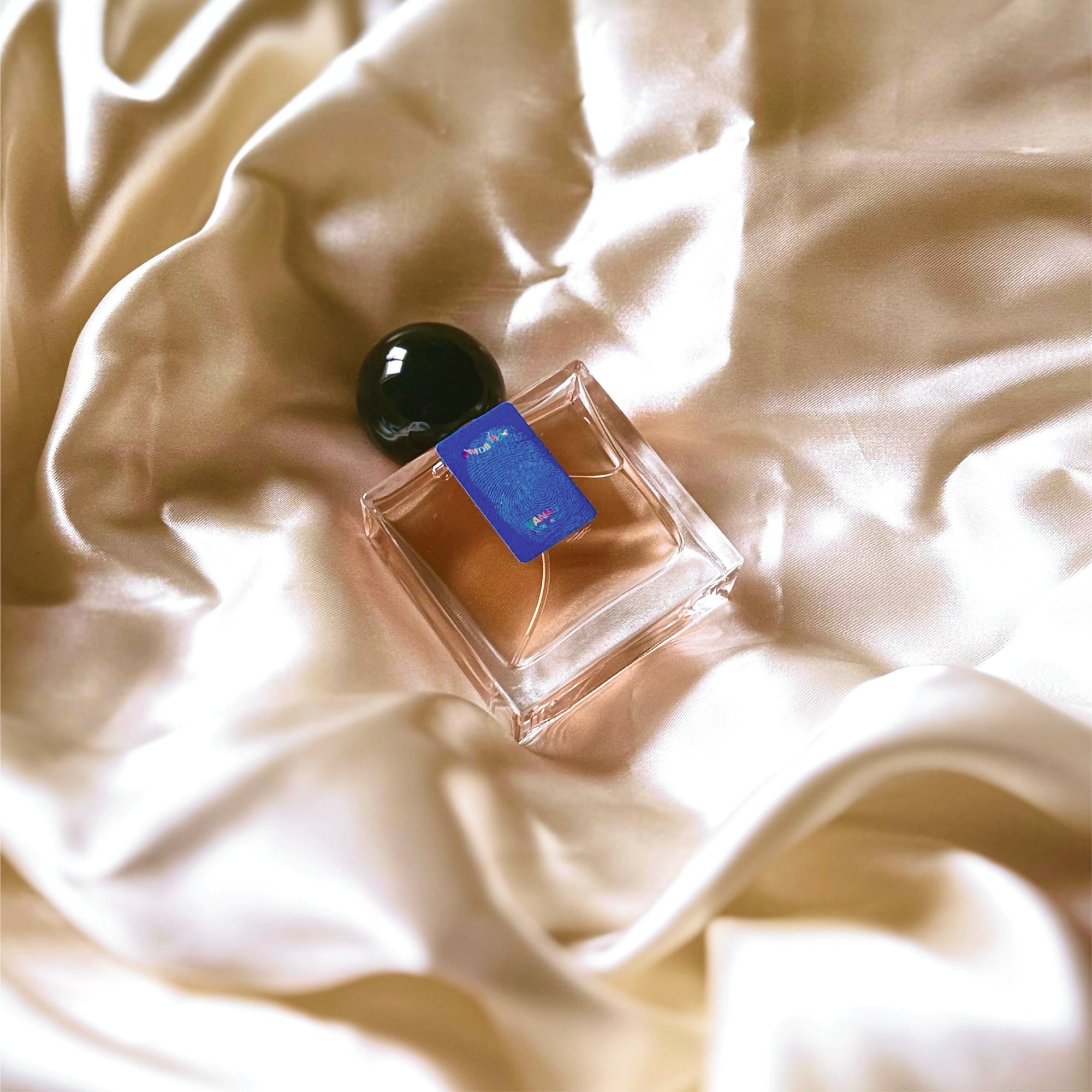 A 30mL bottle of Nanas Eau de Parfum by Chronotope Perfume, nestled in glistening cream, shiny fabric.