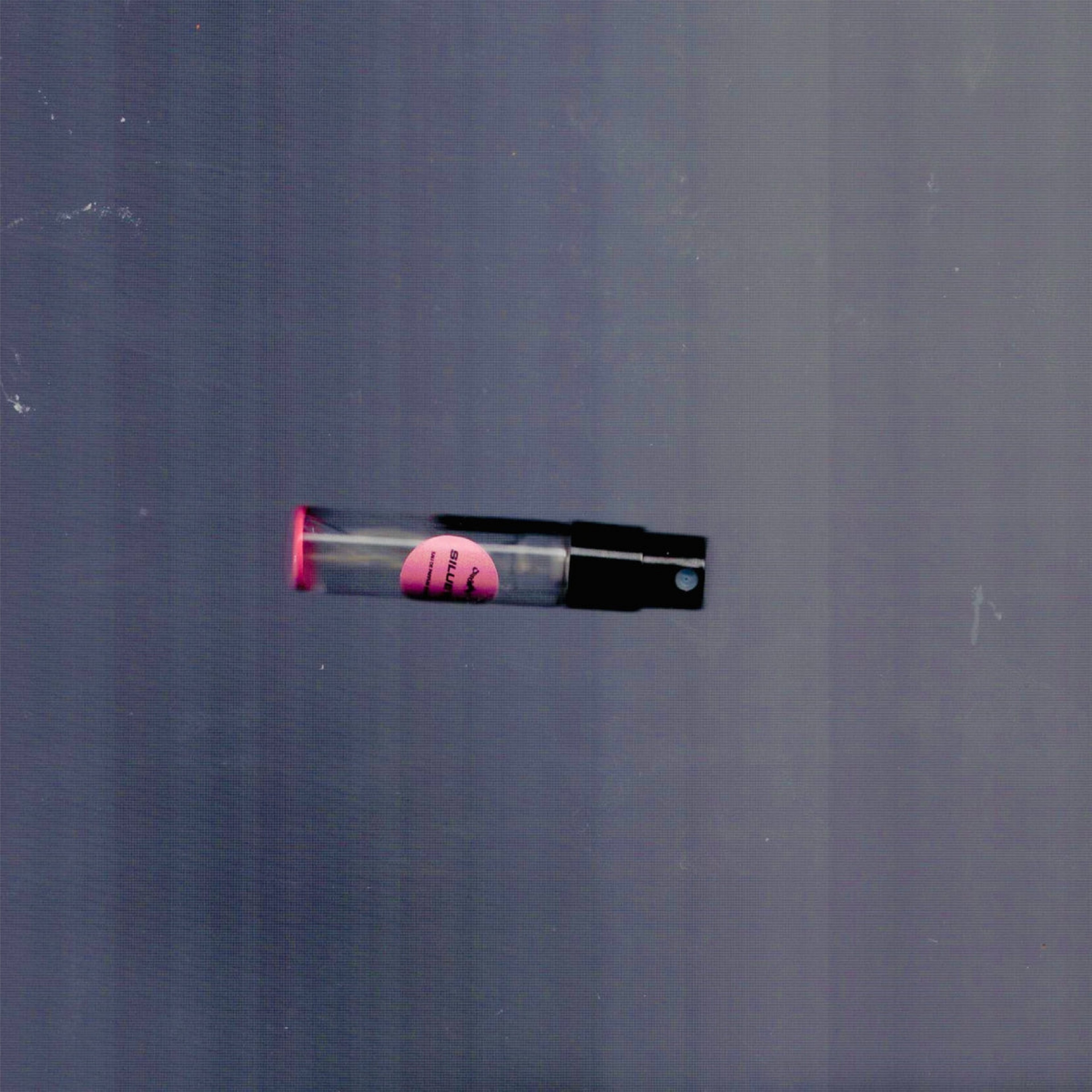 2mL spray sample of Chronotope Perfume’s Silueta Eau de Parfum with Exile Red label and matching enameled tip, lying on a textured gray surface.
