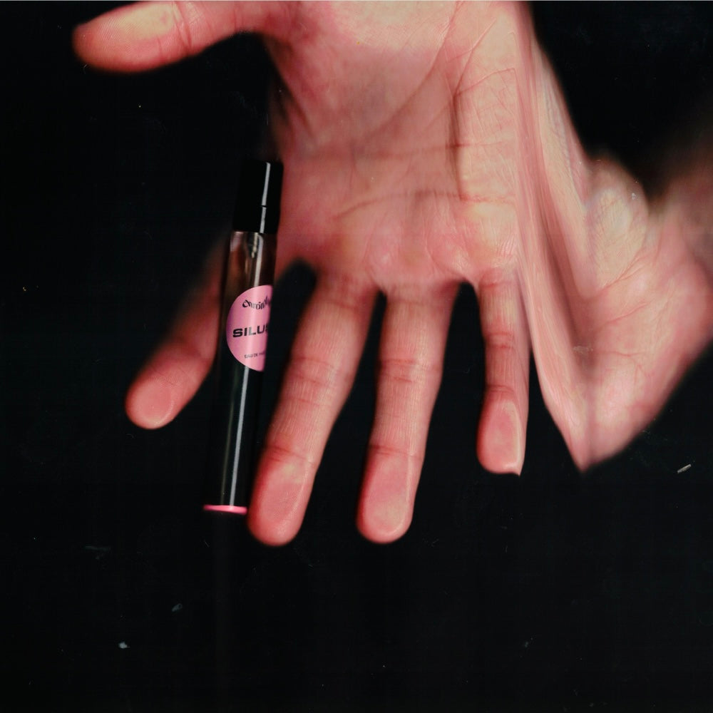 Hand holding a 7.5 mL travel spray of Chronotope Perfume’s Silueta Eau de Parfum, an avant-garde perfume featuring notes of rose, magnolia, and soil that together evoke the scent of loss and exile.