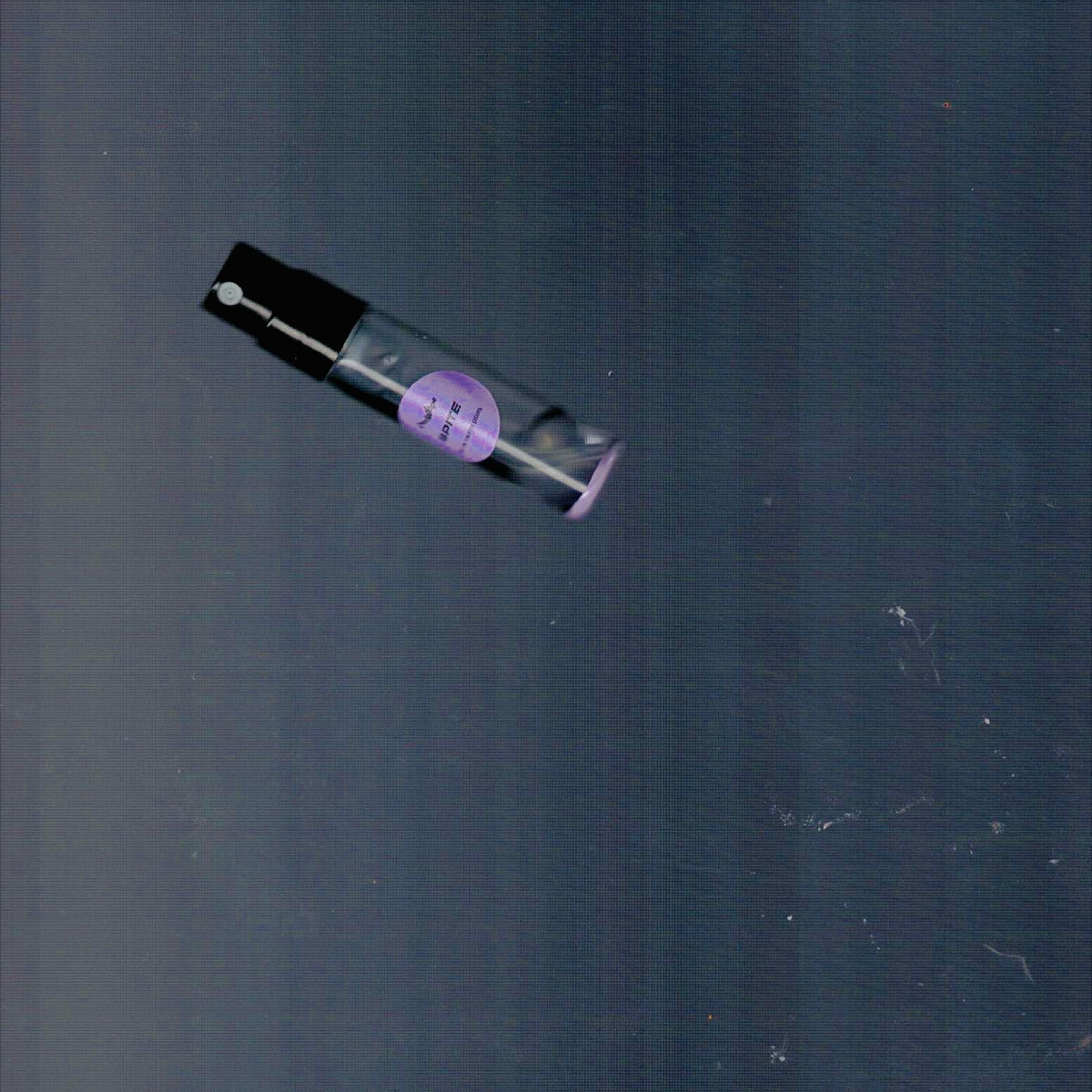2mL spray sample of Chronotope Perfume’s Spite Eau de Toilette with mauve label and matching enameled tip, photographed on a dark blue-gray background.