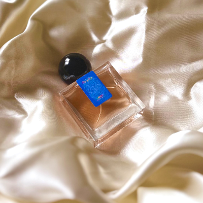 A 30mL bottle of Nanas Eau de Parfum by Chronotope Perfume, nestled in cream, shiny fabric.