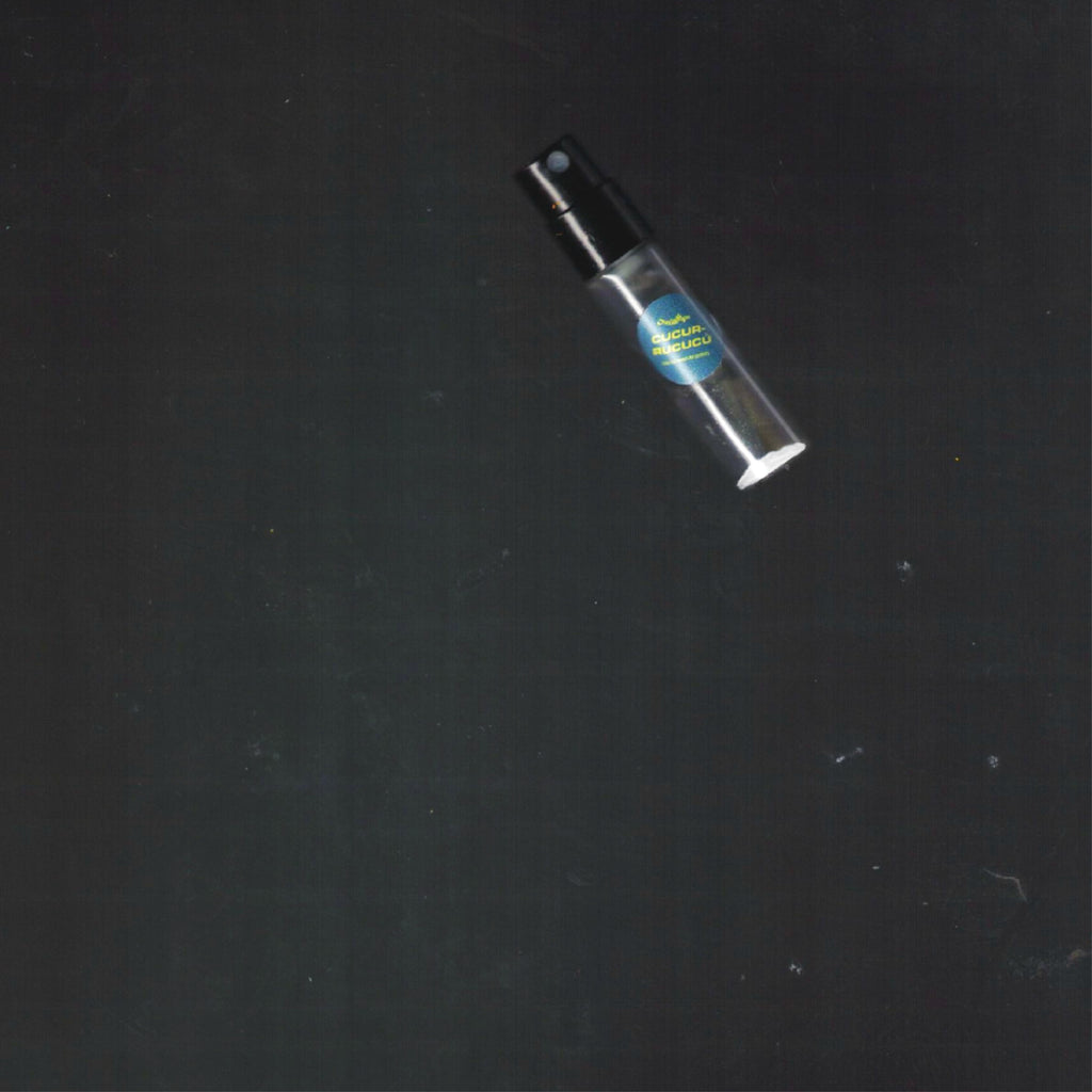 2mL spray sample of Chronotope Perfume’s Cucurrucucú Eau de Parfum with a hunter green label and silver enameled tip, set against a deep gray surface.