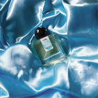 A full, 30mL bottle of Intra Venus Eau de Parfum by Chronotopeis nestled into a nest of colored, silky, shining fabric that matches the color of the thumbprint on the bottle’s label.