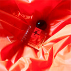 A 30mL bottle of Me/dea Eau de Parfum by Chronotope Perfume is nestled into a background of crinkled, fluorescent orange vinyl in an image showcasing the physical product.