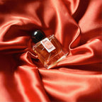 A 30mL bottle of Playalinda Eau de Parfum by Chronotope Perfume. It is nestled in shiny, silky fabric that matches the burnt orange color of the thumbprint on the bottle’s label. 