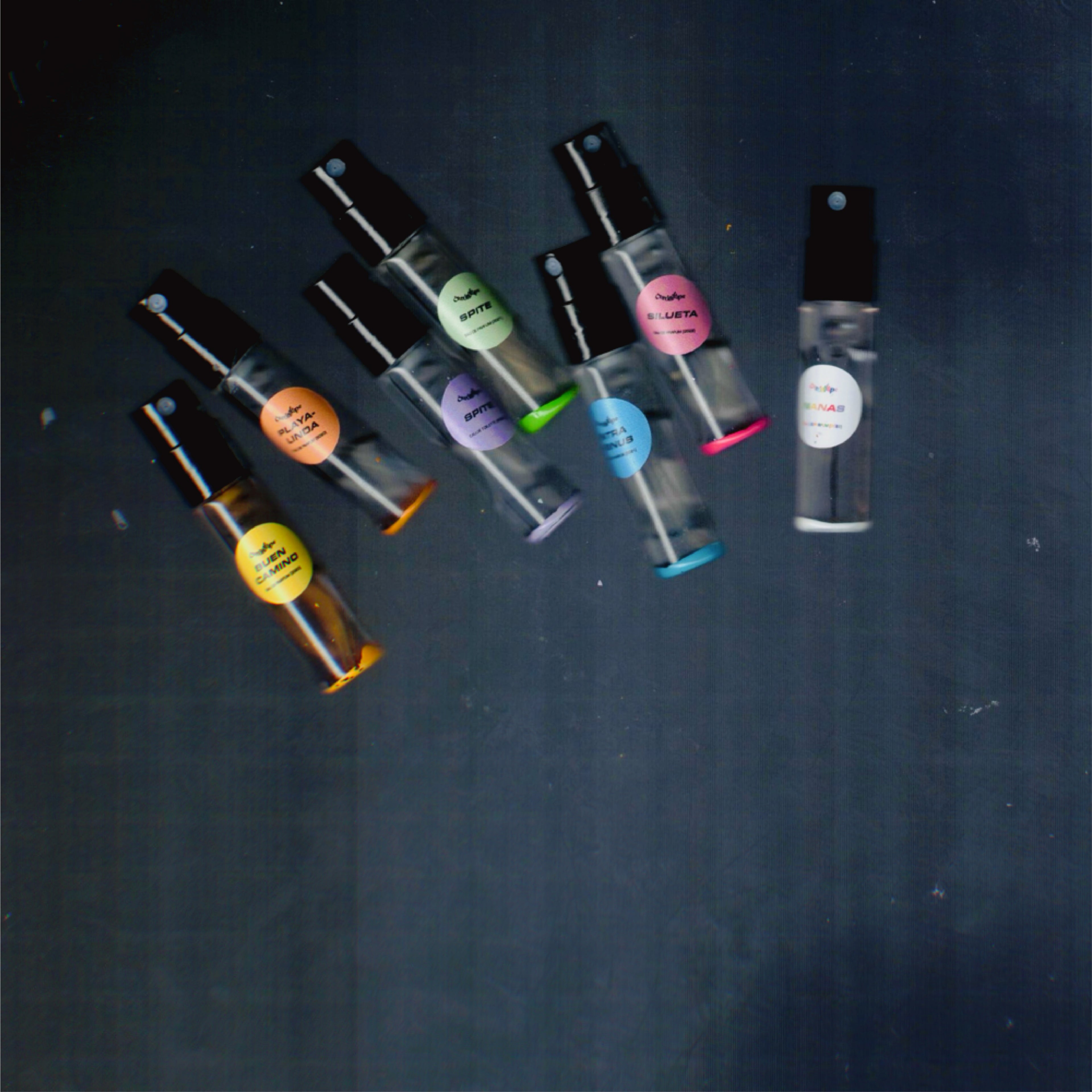Seven Chronotope perfume 2mL sample spray vials for Buen Camino EdP, Playalinda EdP, Spite EdT, Spite EdP, Intra Venus EdP, Silueta EdP, and Nanas EdP, marked in colored enamel and labels.