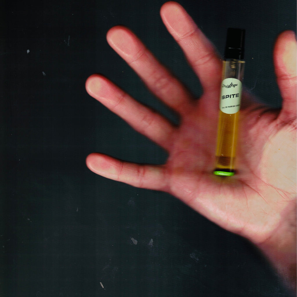 Hand holding a 7.5 mL travel spray of Chronotope Perfume’s Spite Eau de Parfum, a striking, contemporary avant-garde creation — the world’s first artichoke perfume featuring notes of galbanum, rose thorn, jasmine, white rose, fire, allspice, and isobutyl quinoline.