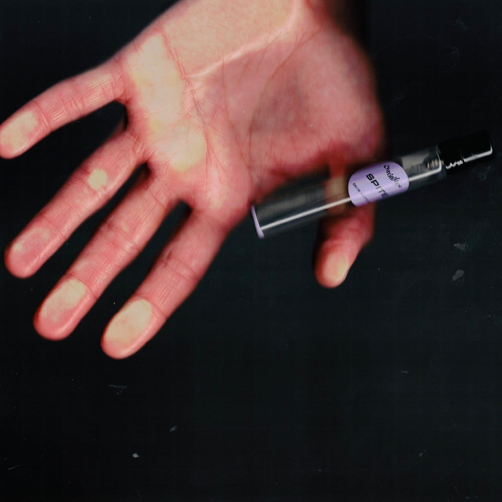 Hand holding a 7.5 mL travel spray of Chronotope Perfume’s Spite Eau de Toilette, an avant-garde, melancholic fragrance featuring notes of rose, ash, violet leaf, sandalwood, leather, scalded sugar, and fog.