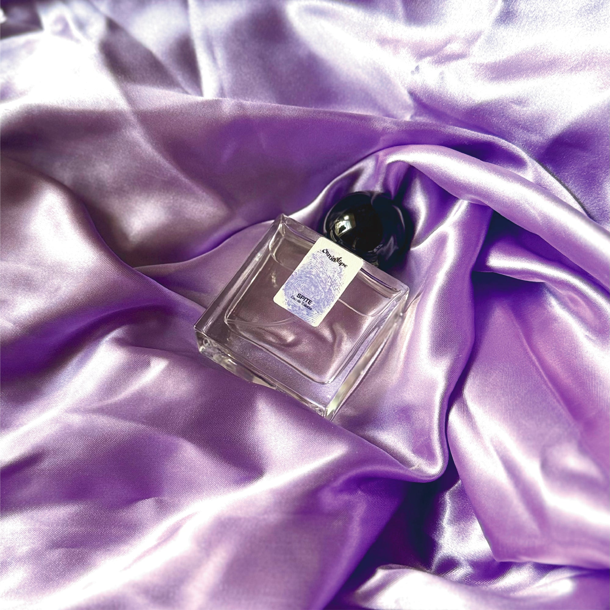 Chronotope perfume’s Spite EdT lies in a shimmering nest of fabric in the same mauve color as the thumbprint on the perfume bottle’s label.