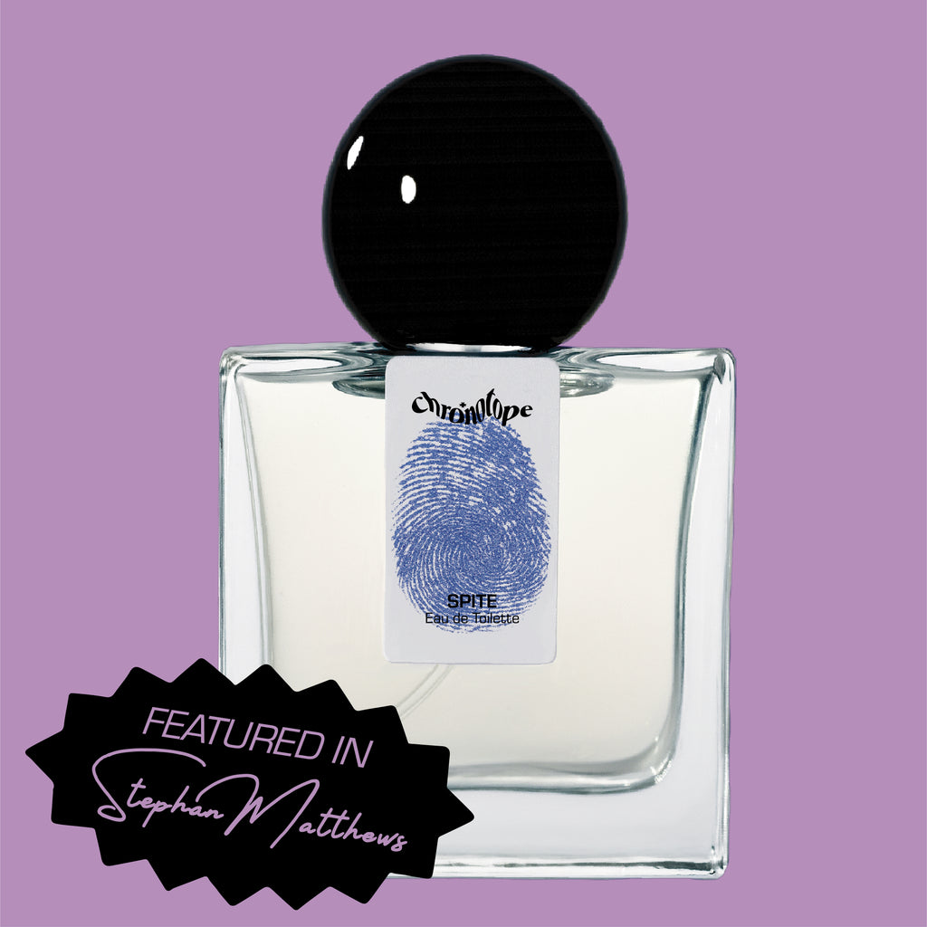 Digital rendering of Chronotope Perfume’s Spite Eau de Toilette bottle with a white label stamped with the perfumer’s thumbprint in Melancholic Mauve, containing pale violet-gray perfume, and set against a matching Melancholic Mauve background with a badge noting press coverage in Stephan Matthews.