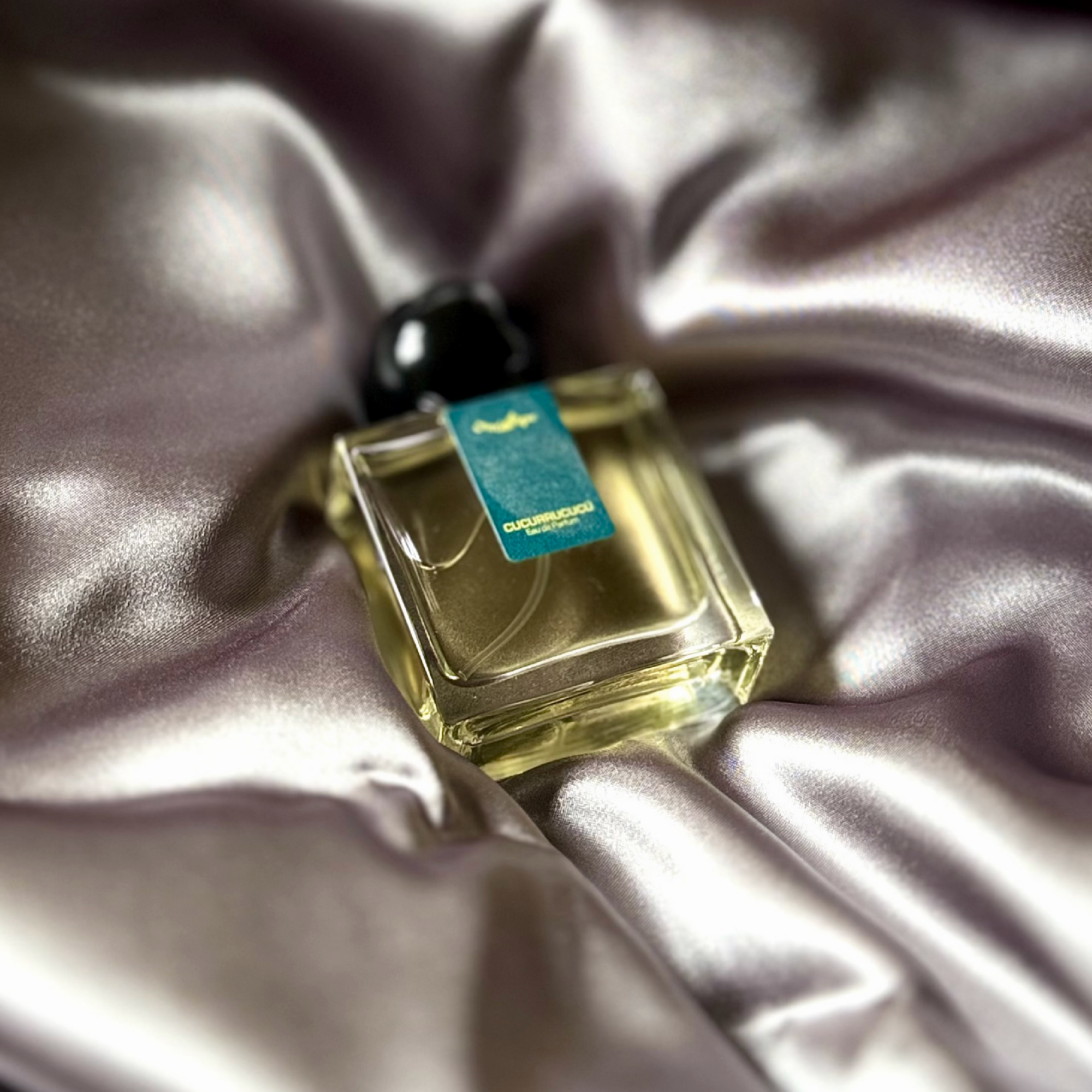 Chronotope perfume’s Cucurrucucu EdP lies in a shimmering nest of fabric in the same gunmetal silver-grey color as the thumbprint on the perfume bottle’s label.