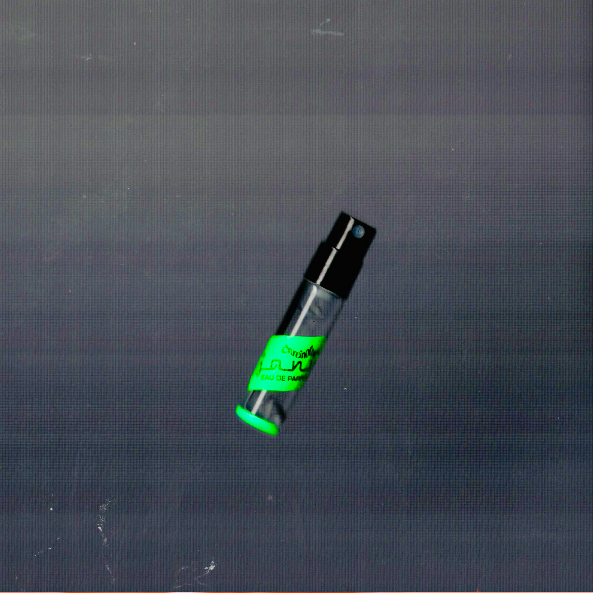 A 2mL spray sample vial of Janus EdP by Chronotope Perfume is depicted floating against a gradient grey void full of tiny multicolored scan lines and other digital imagery defects.