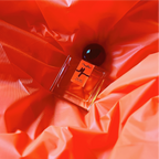 A 30mL bottle of Me/dea Eau de Parfum by Chronotope Perfume is nestled into a background of crinkled, fluorescent orange vinyl in an image showcasing the physical product.